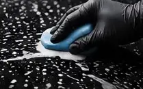 Gloved hand using a clay bar on wet black paint