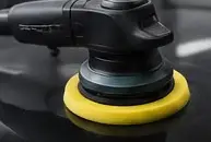 Dual-action polisher with a yellow pad on black paint